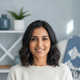 Headshot portrait of a smiling South Asian woman in her late 30s, conveying trust and happiness.